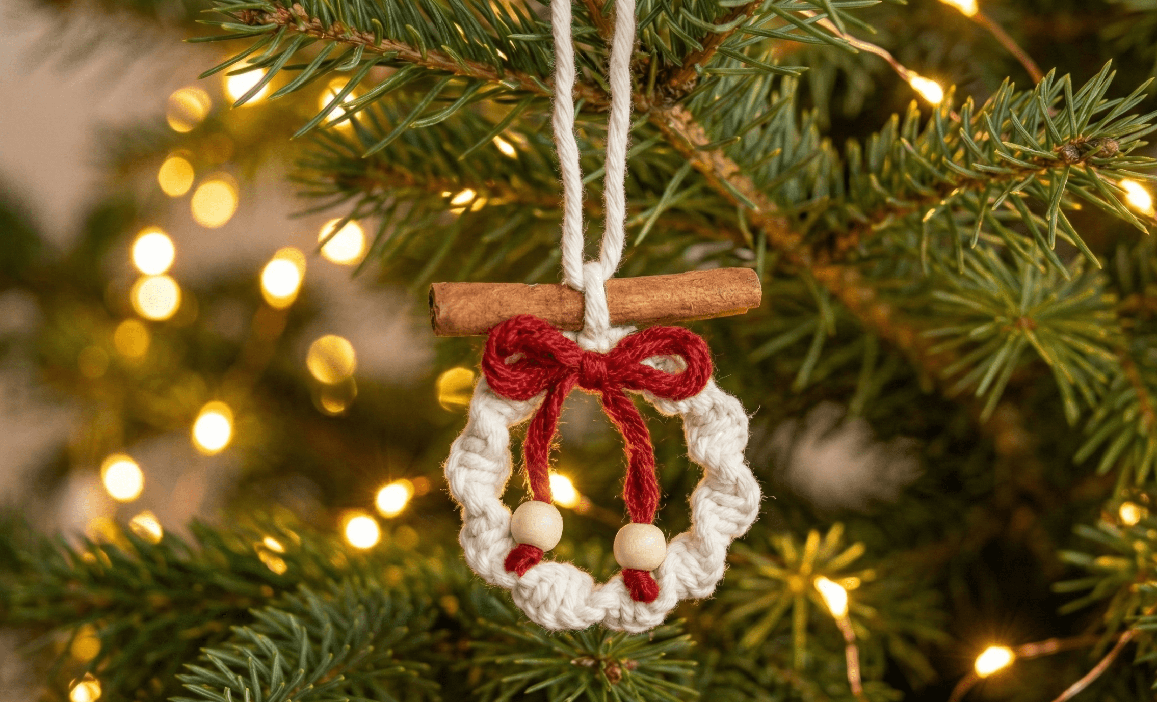 Mini macrame wreath Christmas ornament made with white and red cotton cord, cinnamon stick, and wooden beads hanging on a Christmas tree